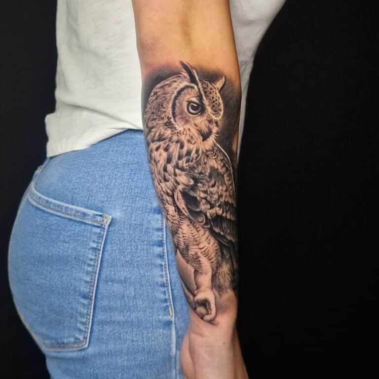 Realistische uil tattoo in zwart-wit op de onderarm.