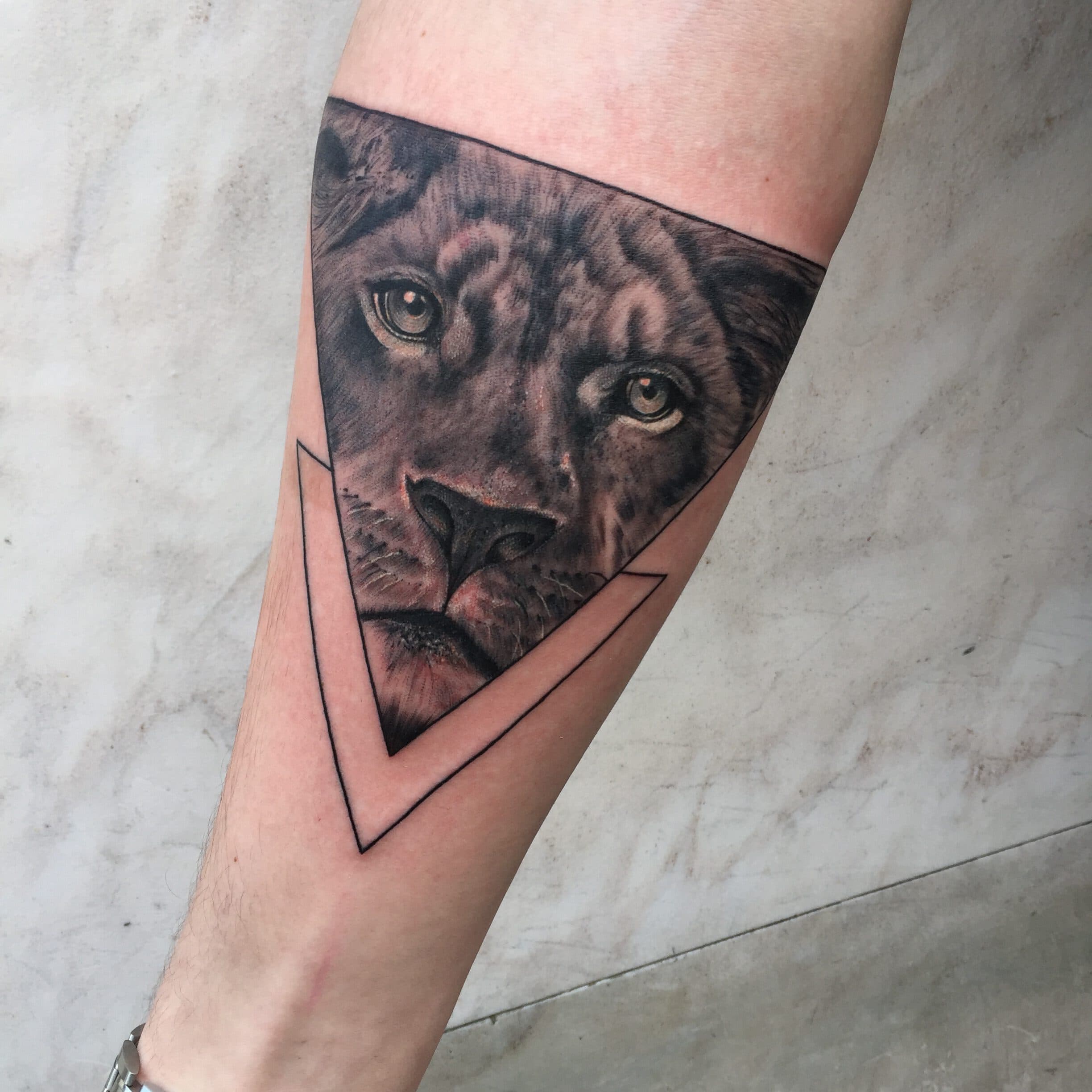 Realistische leeuwin in een geometrische driehoek op de onderarm.