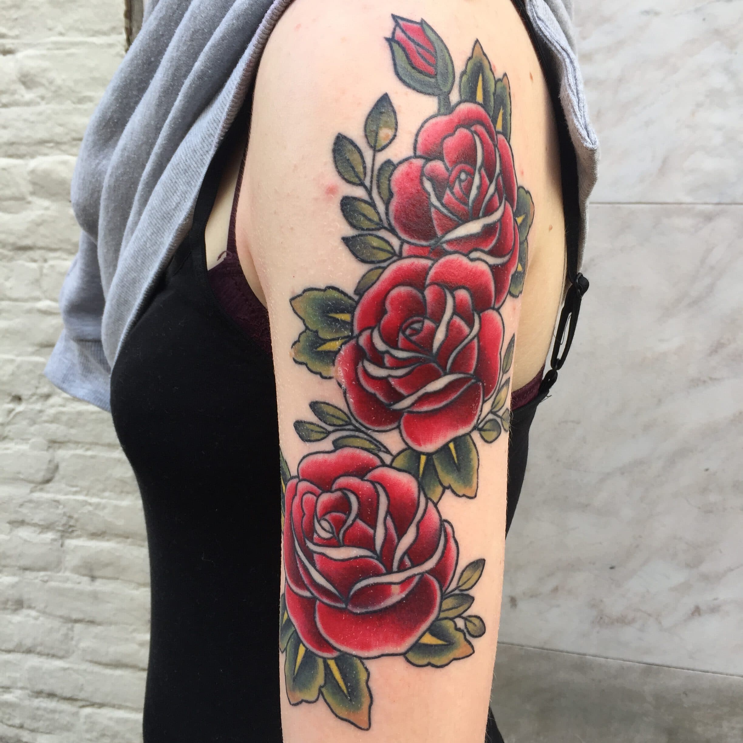 Traditionele tattoo van drie rode rozen met bladeren op de bovenarm.