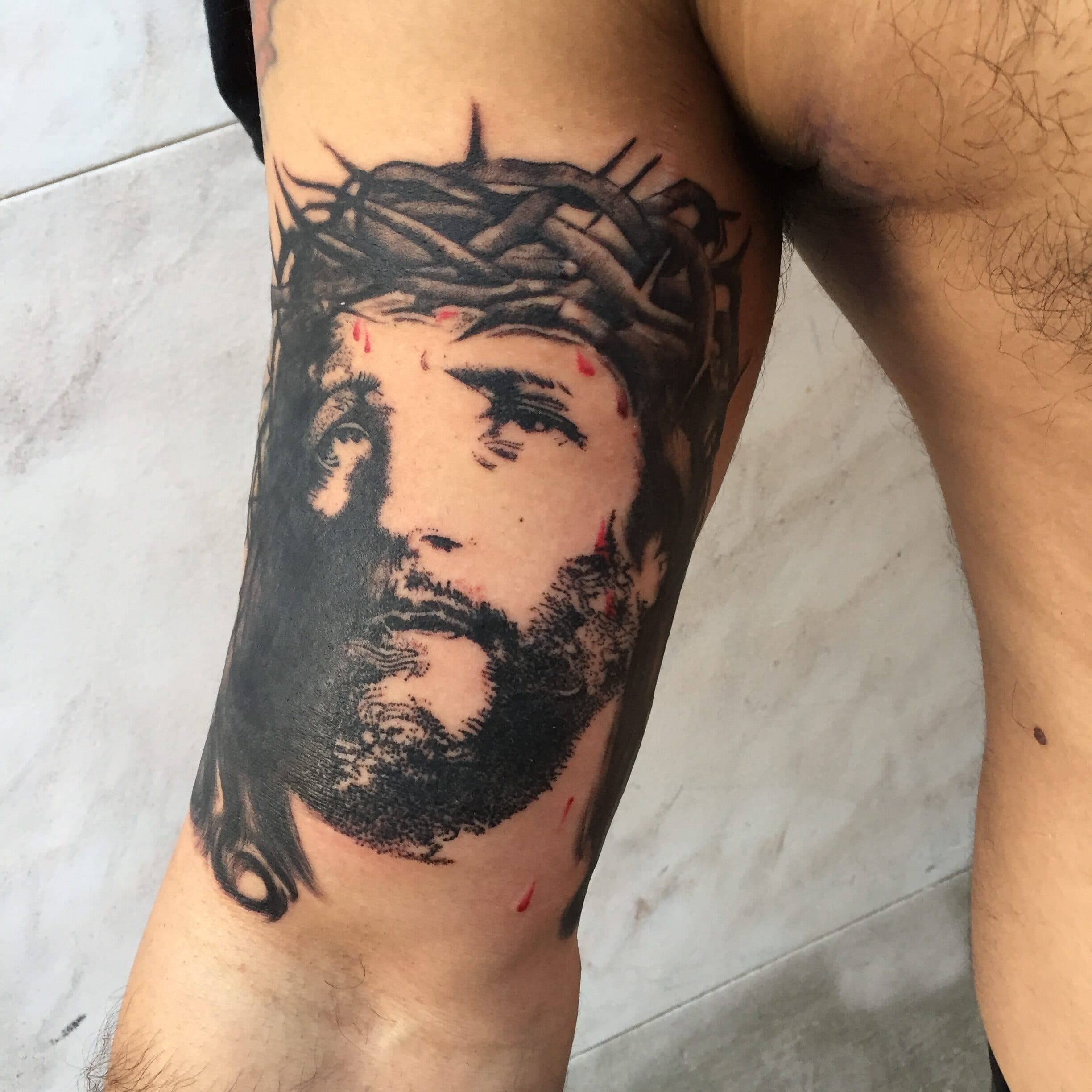 Realistisch portret van Jezus met doornenkroon op de bovenarm.