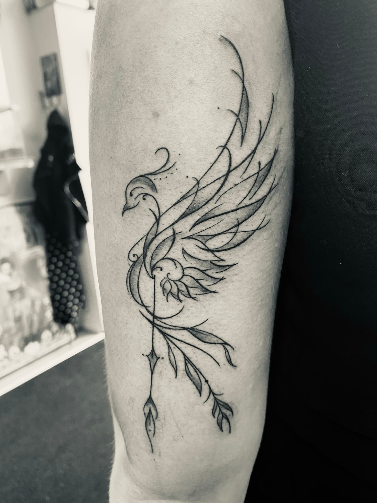 Elegante fineline feniks of vogel met vloeiende lijnen en bladeren op bovenarm