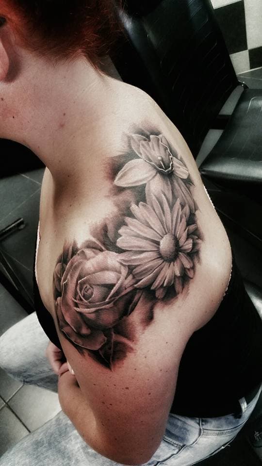 Zwart-wit bloemen tattoo op schouder met roos, madeliefje en narcis.