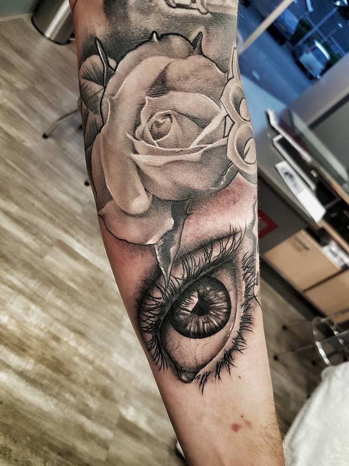 Realistische zwart-wit tattoo van een roos en een oog op de onderarm.