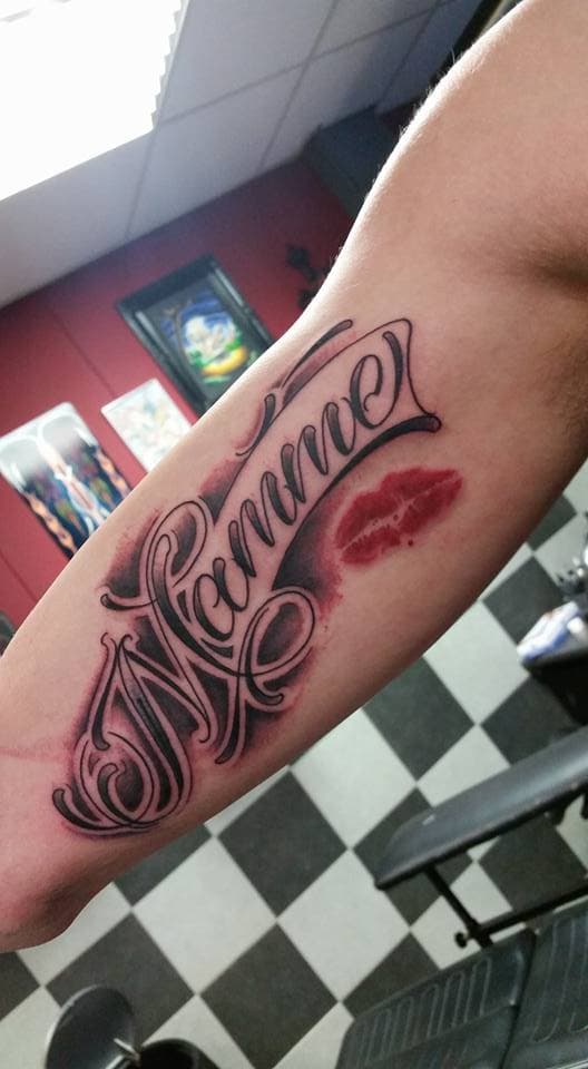 Lettering tattoo 'Mamme' met rode lippenstift kus op de bovenarm.