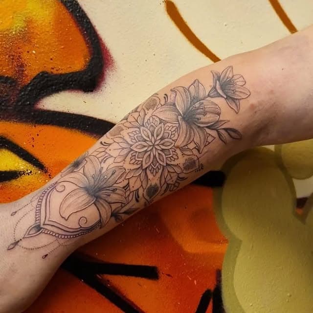 Zwart-wit tattoo van lelies en een mandala op de onderarm.