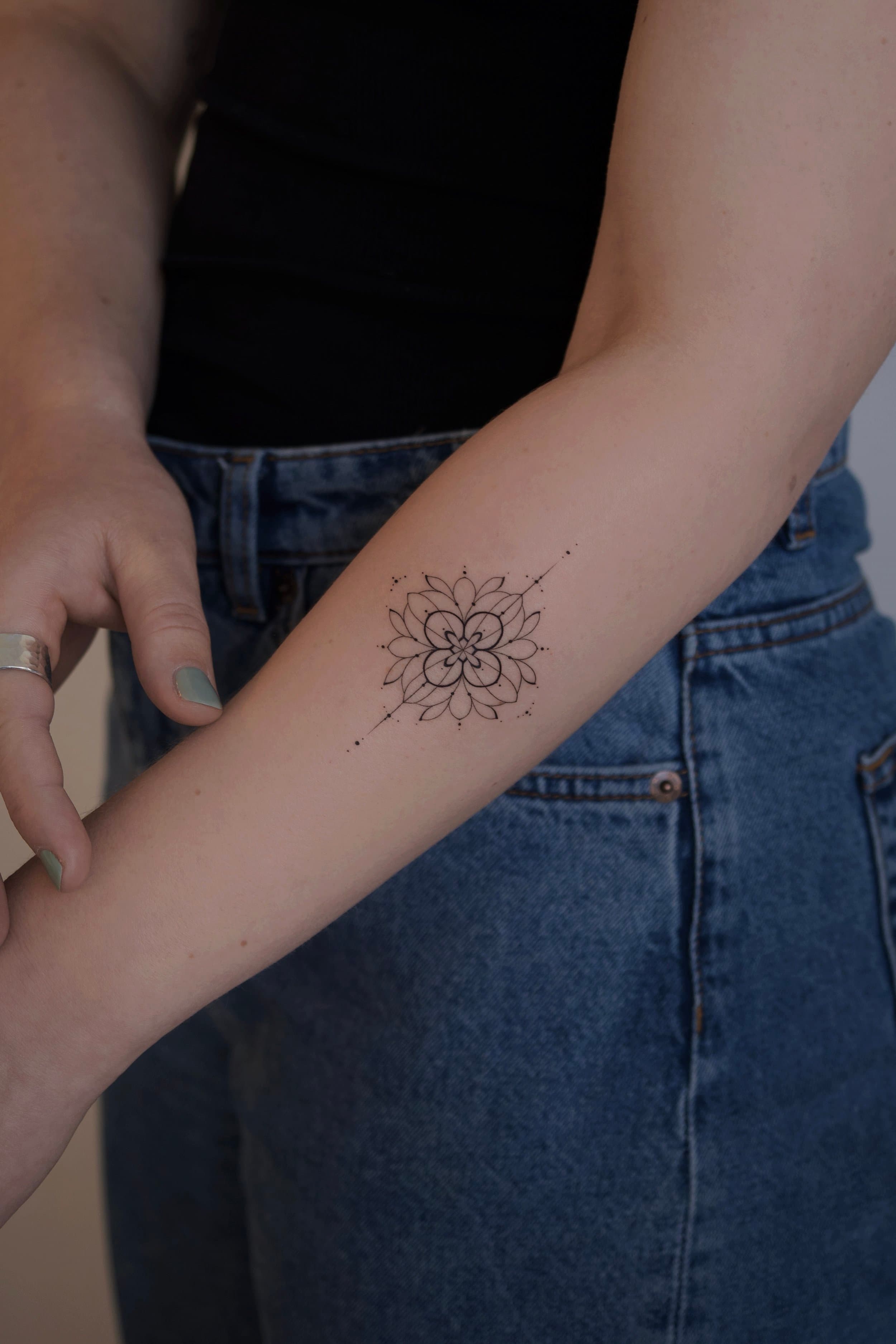Fineline mandala bloem op onderarm.