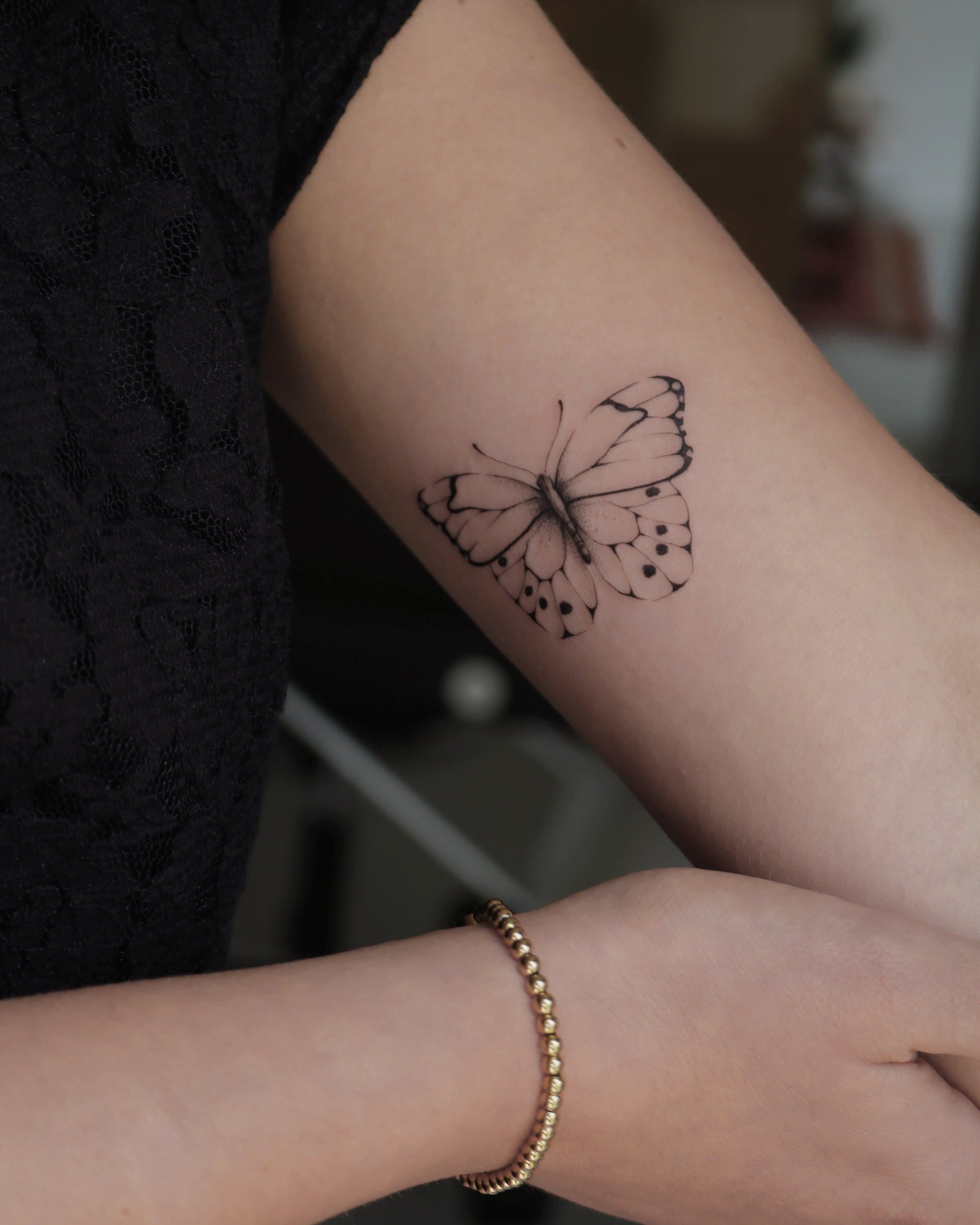Fijne lijnwerk vlinder tattoo op de bovenarm.