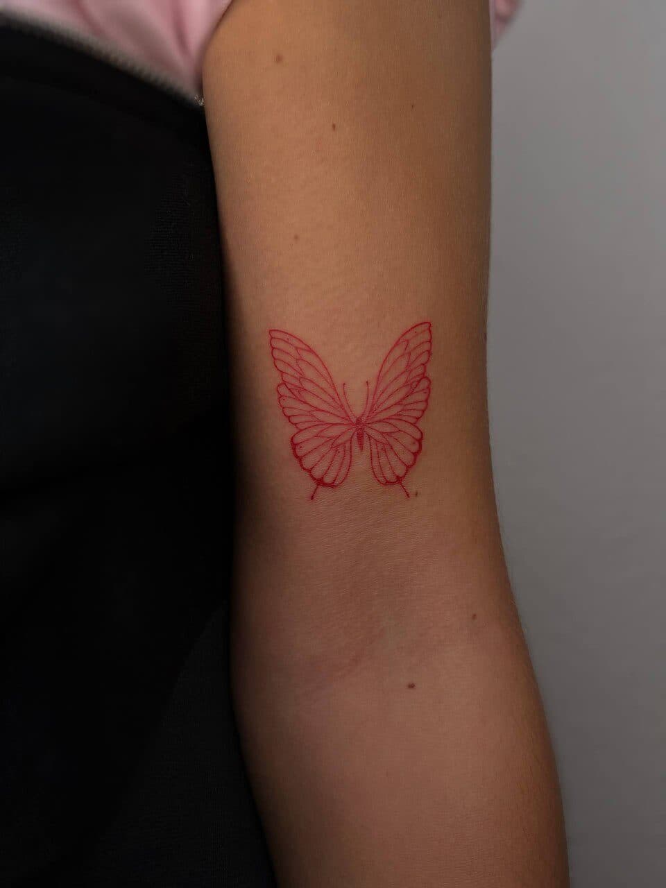 Rode fineline vlinder tattoo op bovenarm