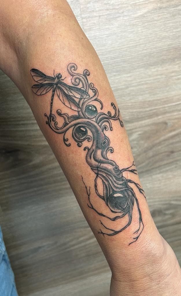 Blackwork tattoo van een libelle op een kronkelende tak met bollen.