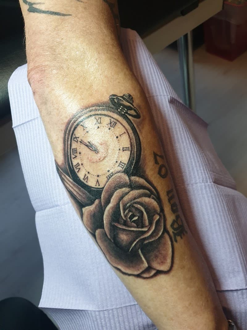 Zwart-wit tattoo van een zakhorloge en een roos op de onderarm.