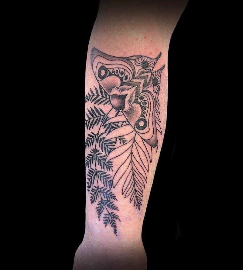 Zwart-wit tattoo van een mot met varenbladeren op de onderarm.