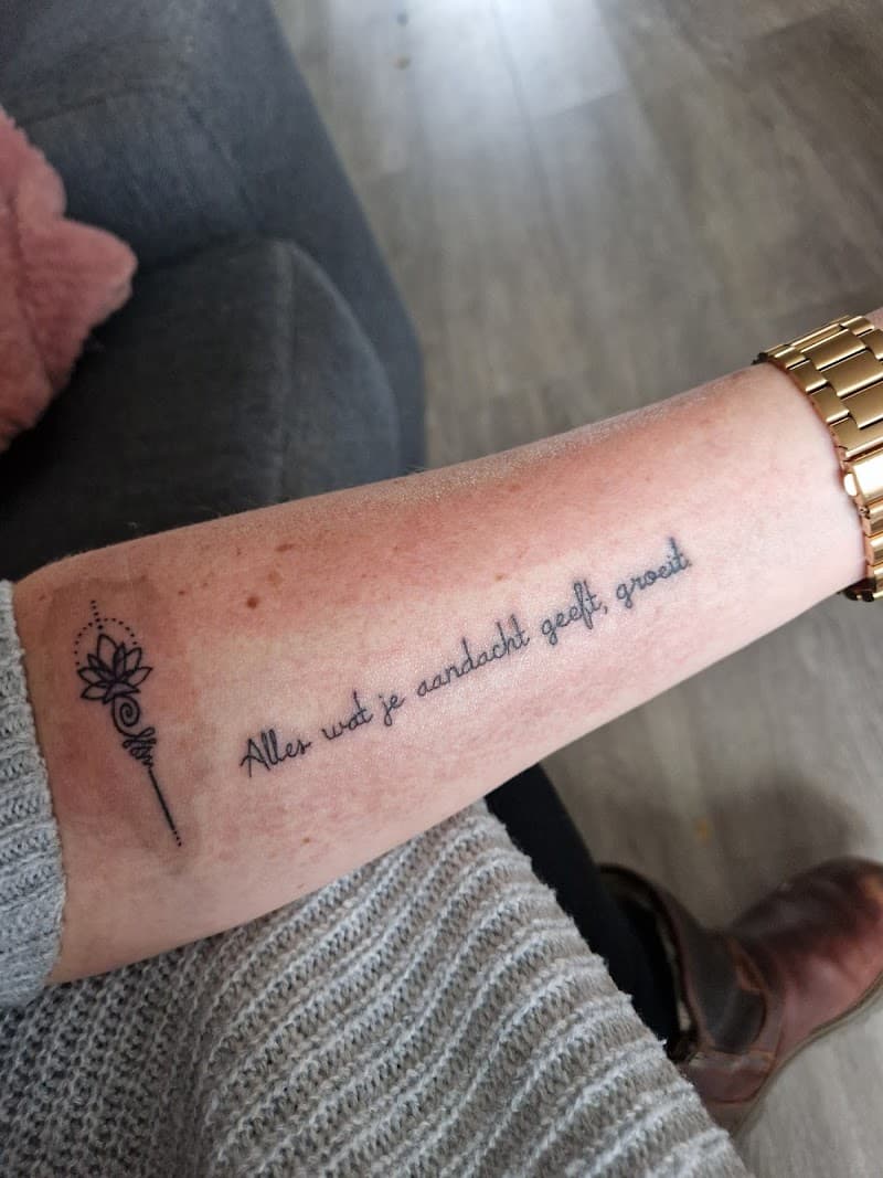 Fineline unalome met lotus en Nederlandse tekst op onderarm.