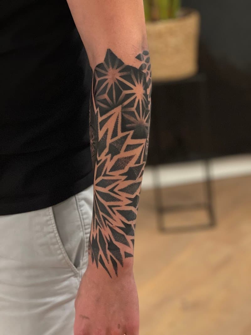 Grote geometrische blackwork tattoo op onderarm met sterren en patronen.