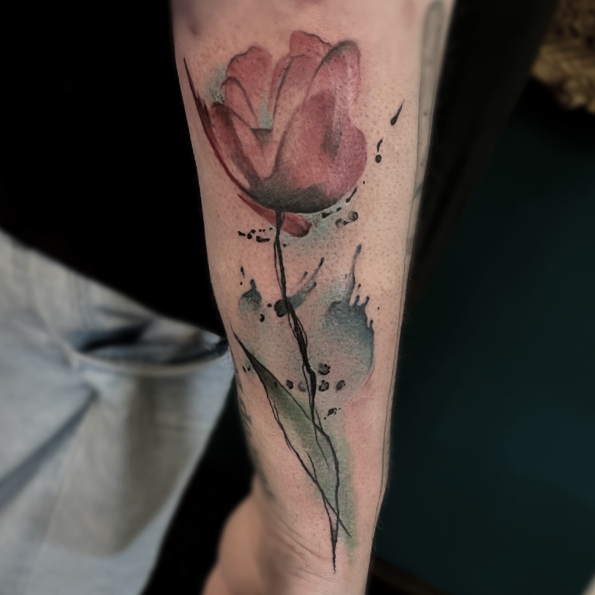 Watercolor tulp tattoo op de onderarm met verfspatten.