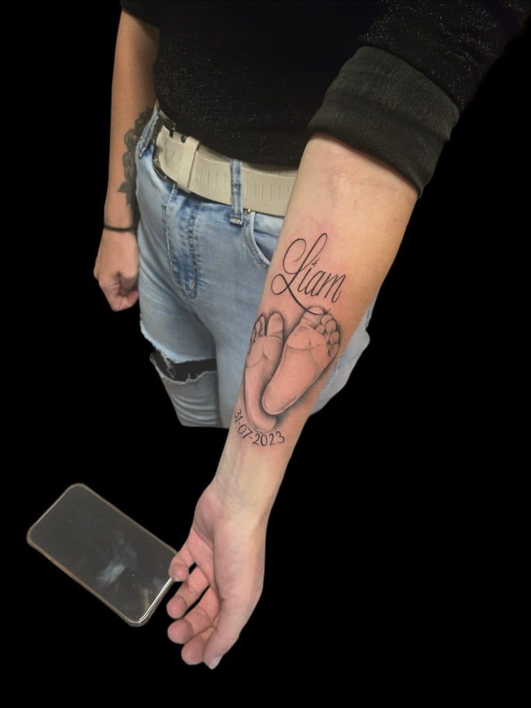 Realistische babyvoetjes met naam 'Liam' en datum op onderarm.