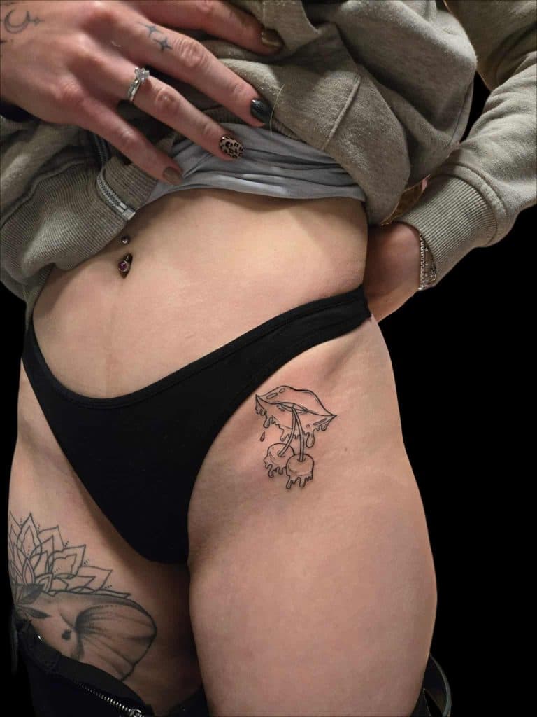 Fineline tattoo van lippen met smeltende kersen op de heup.