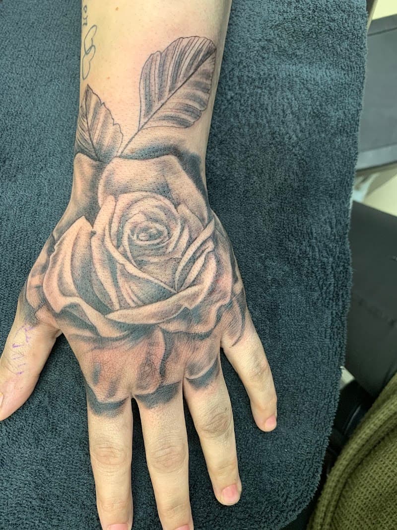 Zwart-wit roos tattoo op de hand met bladeren.