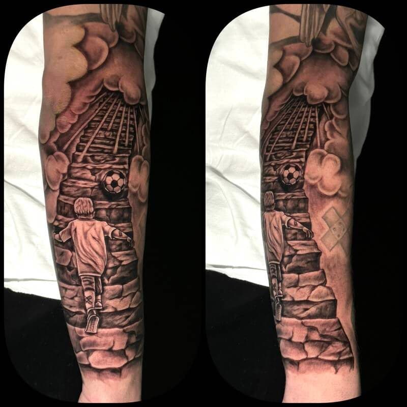 Zwart-wit tattoo van jongen op trap naar voetbal in wolken.
