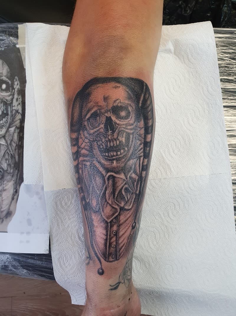 Zwart-wit tattoo van een schedel in een narrenpak op de onderarm.