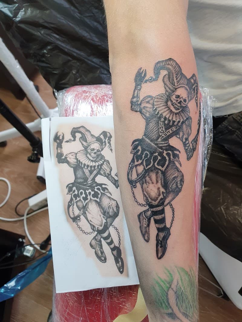 Gedetailleerde zwart-wit tattoo van een dansend skelet in narrenpak op de onderarm.