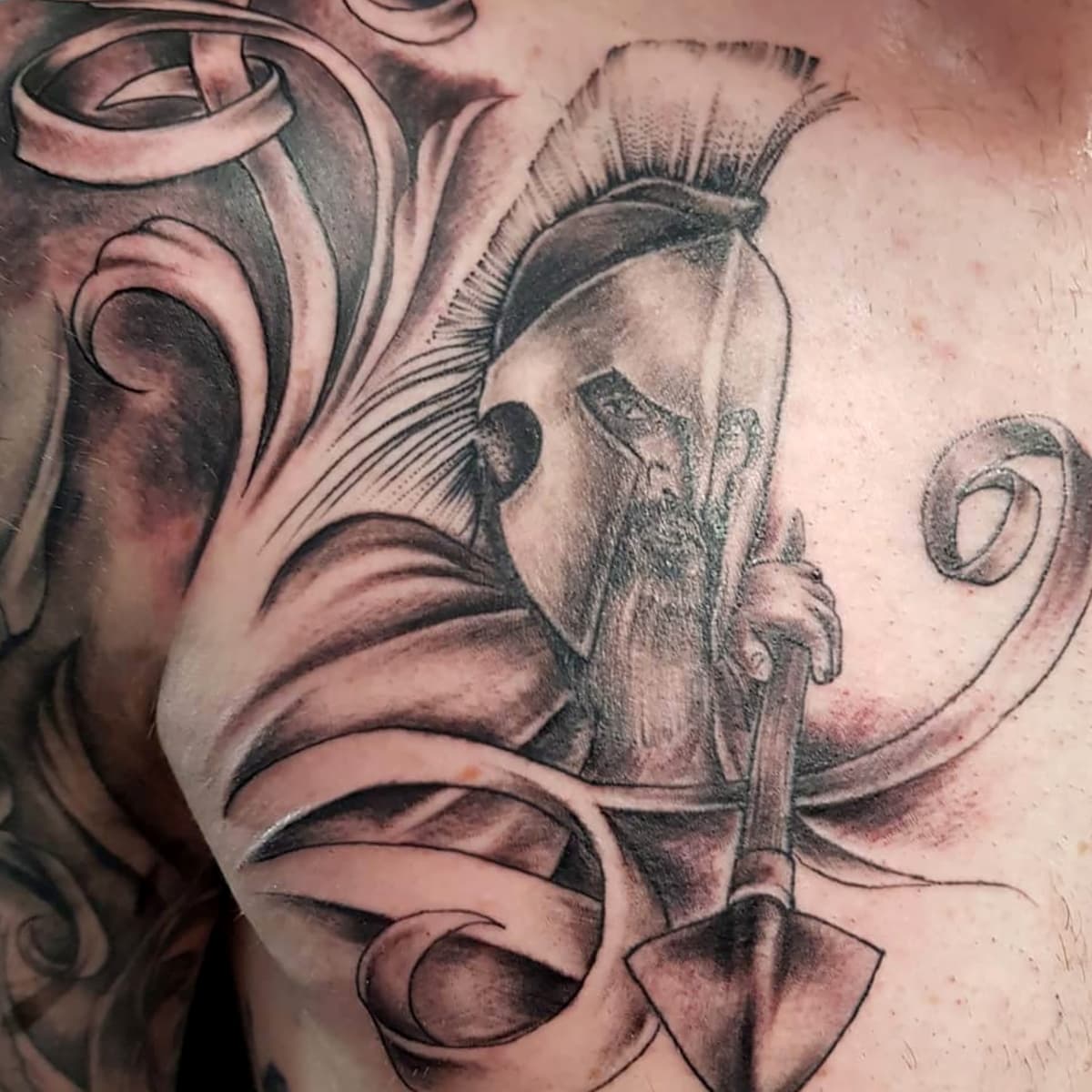 Blackwork tattoo van een Spartaanse krijger met helm en speer op de borst.