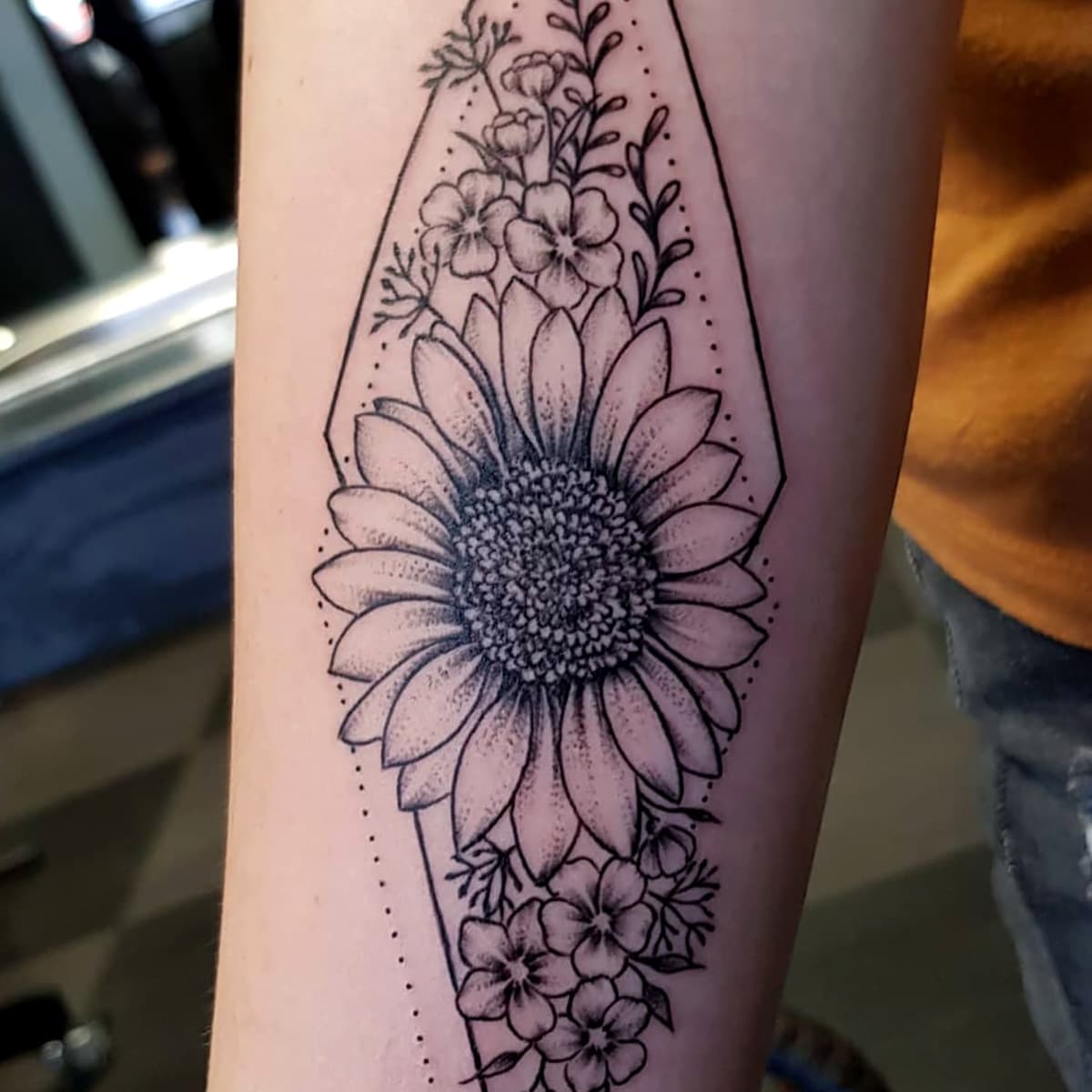 Zonnebloem en bloemen in geometrisch kader op onderarm.