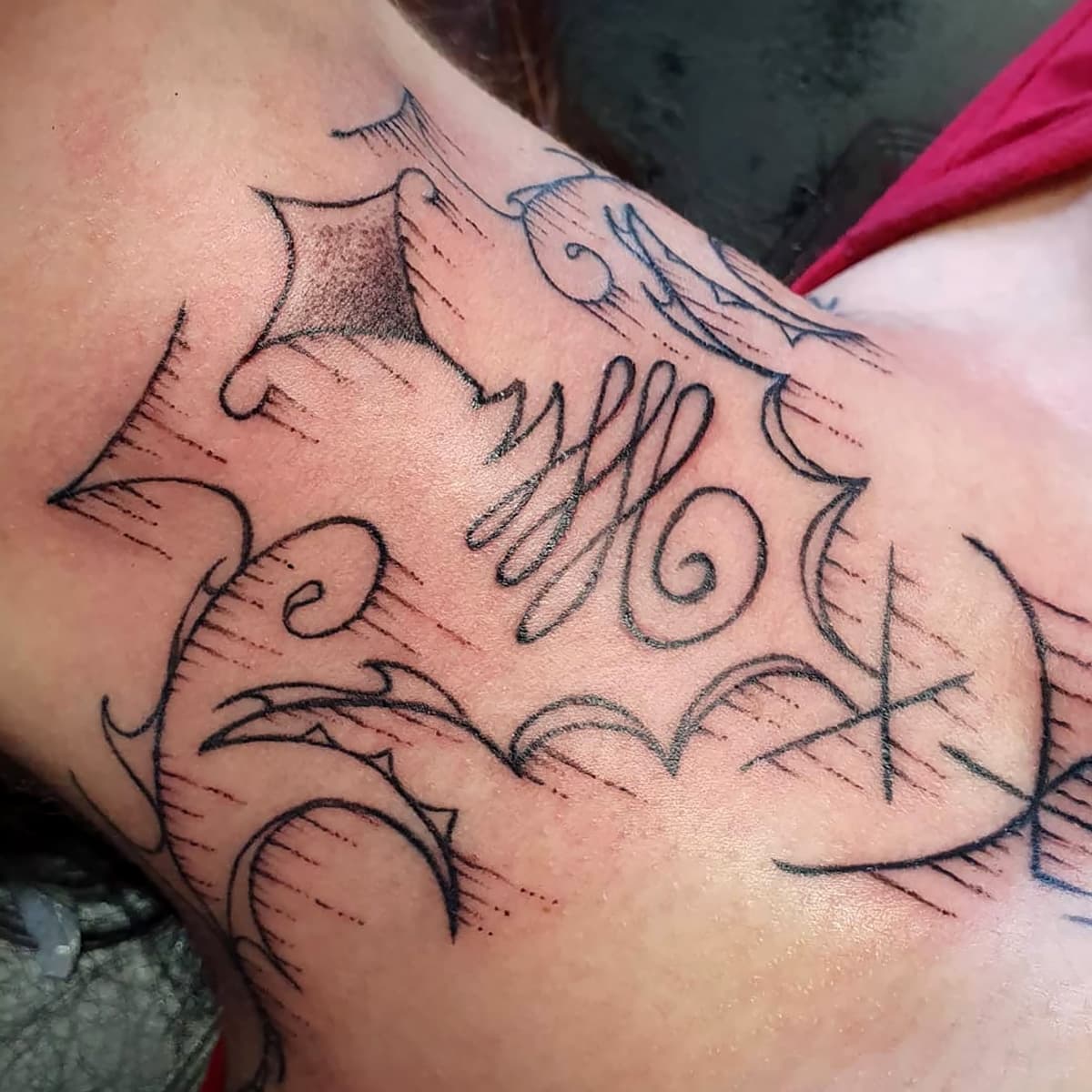 Abstracte zwarte lijnwerk tattoo met scherpe punten en krullen op de bovenarm.