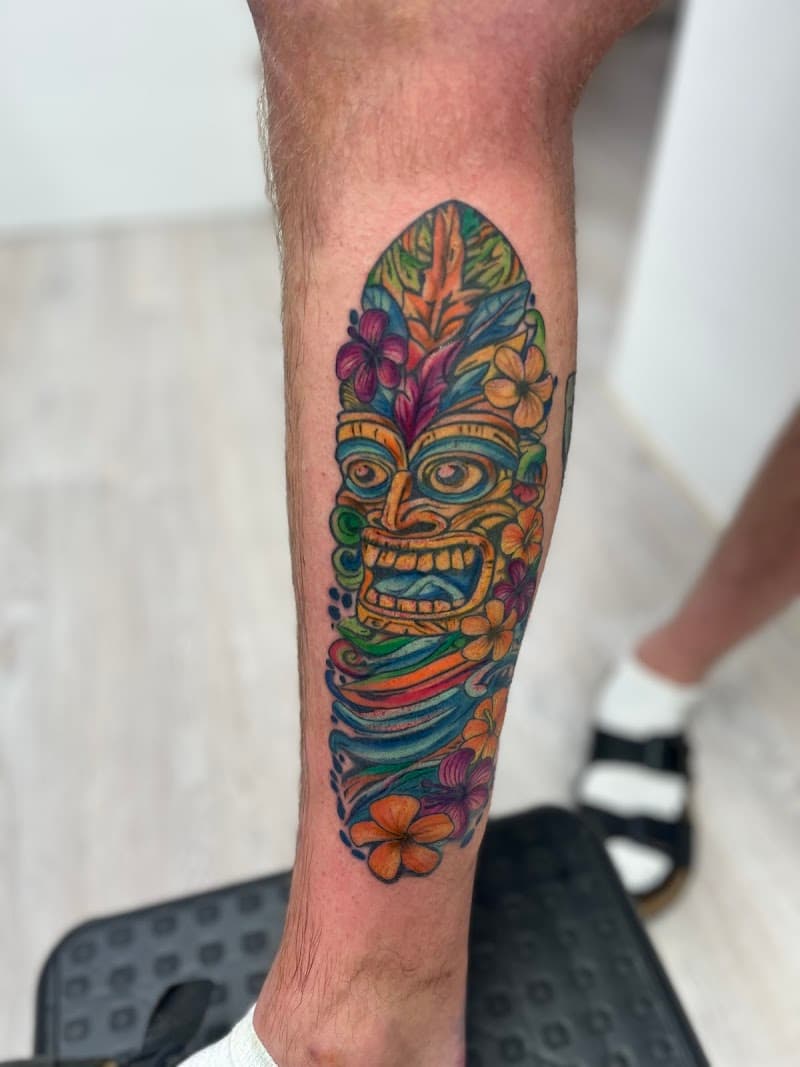 Kleurrijke Tiki masker tattoo met bloemen op onderbeen.