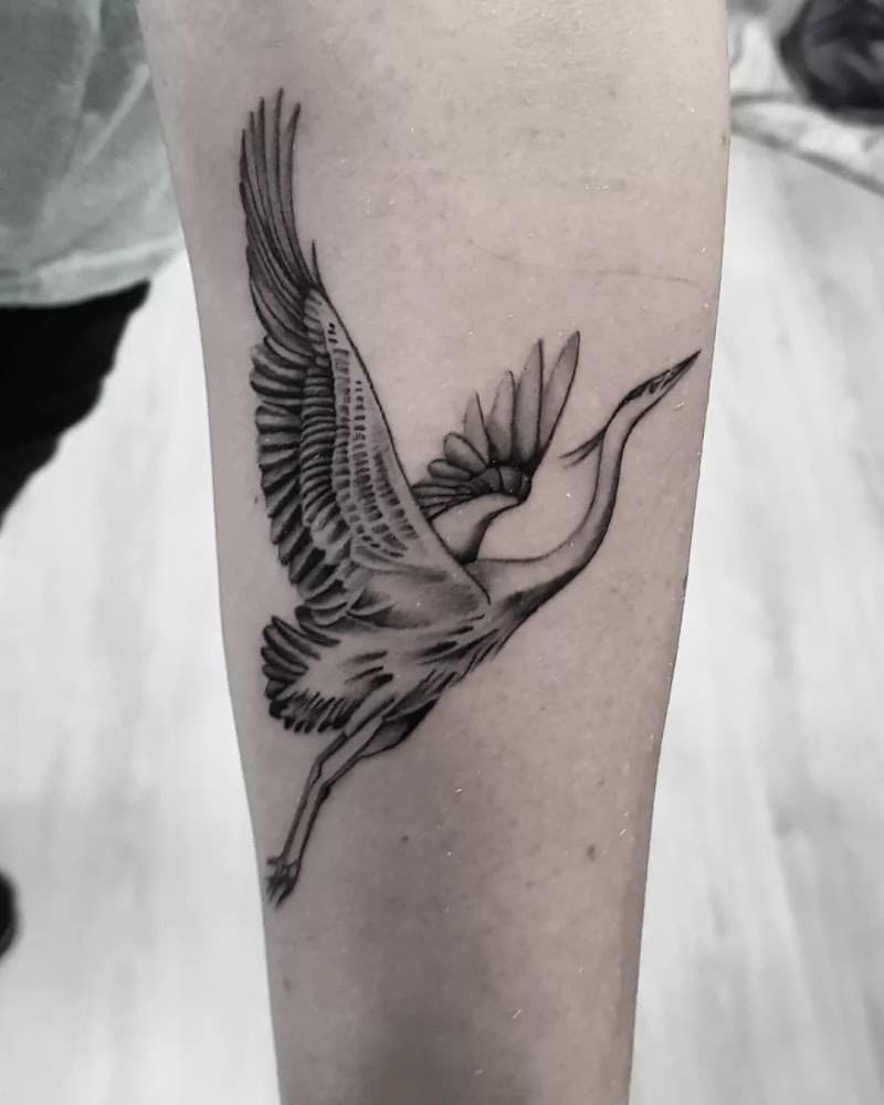 Zwart-wit tattoo van een vliegende reiger op de onderarm.