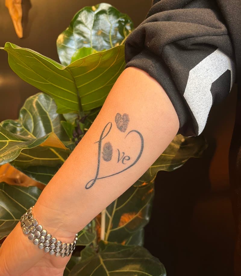 Fineline 'love' tattoo met vingerafdrukken in een hartvorm op de onderarm.