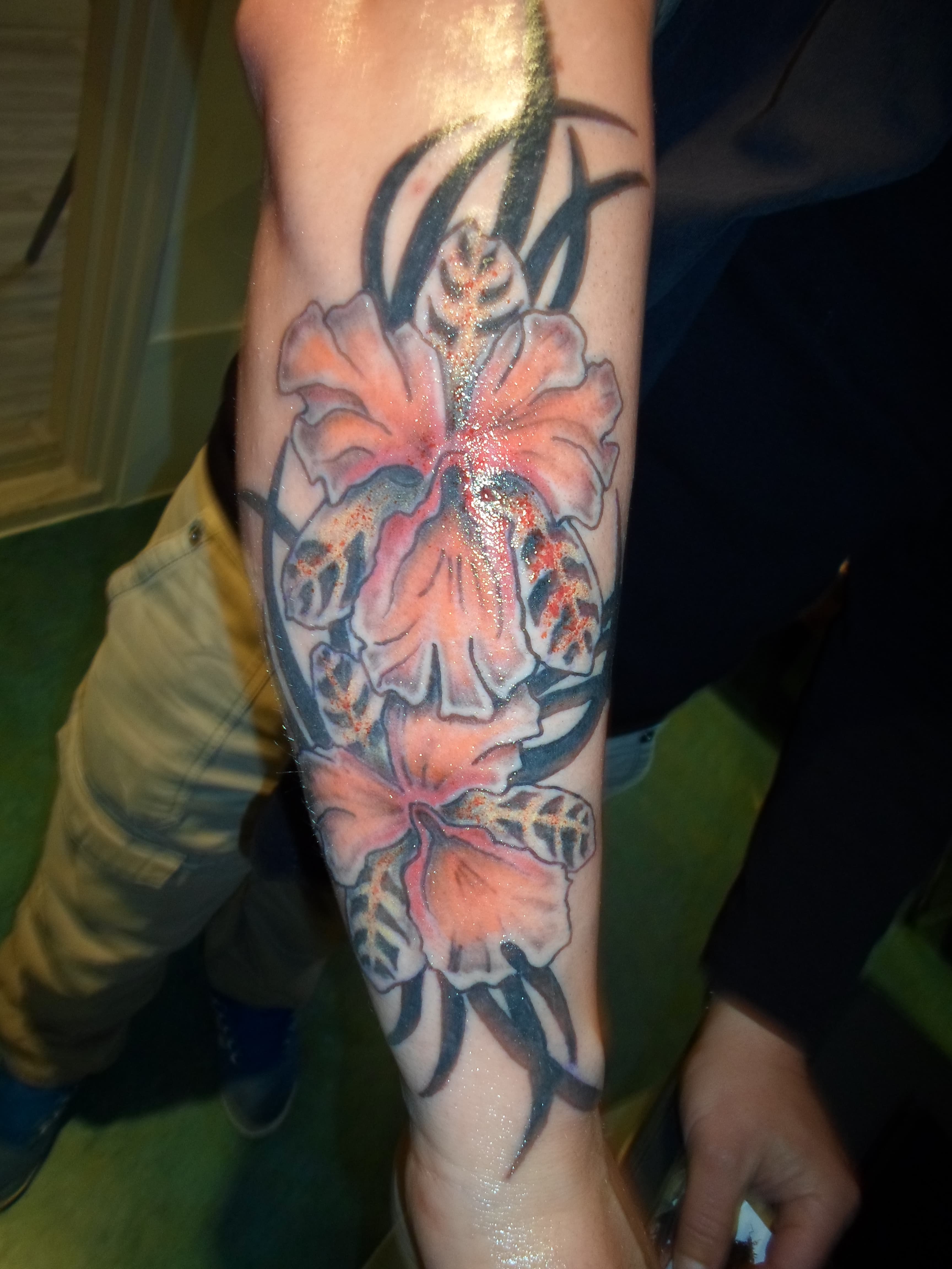 Kleurrijke hibiscus bloemen met zwarte tribal elementen op de onderarm.