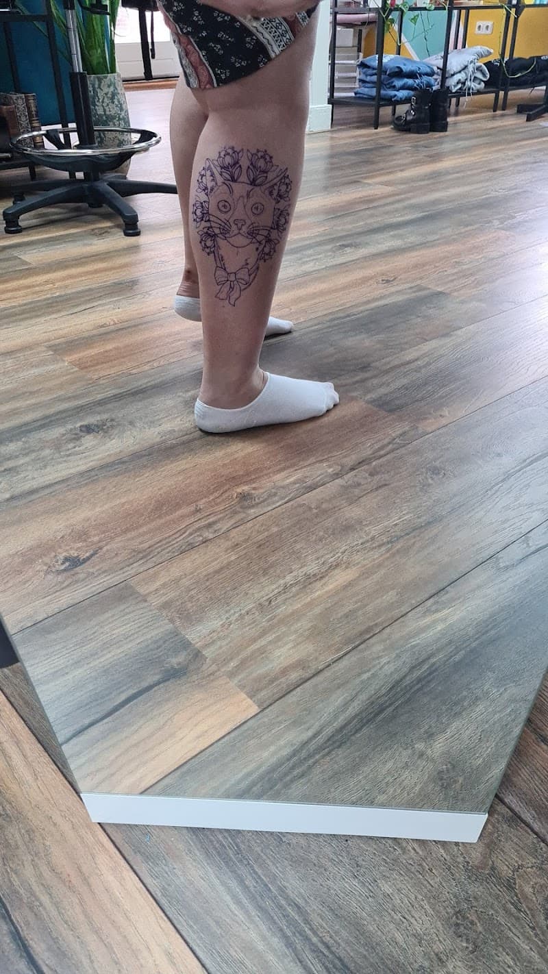 Fineline tattoo van een kattenhoofd met bloemen en een strik op het onderbeen.