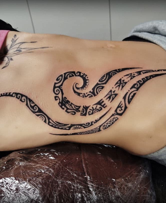 Grote zwarte tribale golf tattoo op de ribben en zij.