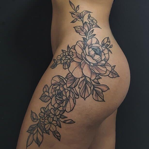 Grote zwart-wit bloemen tattoo op heup en bovenbeen.