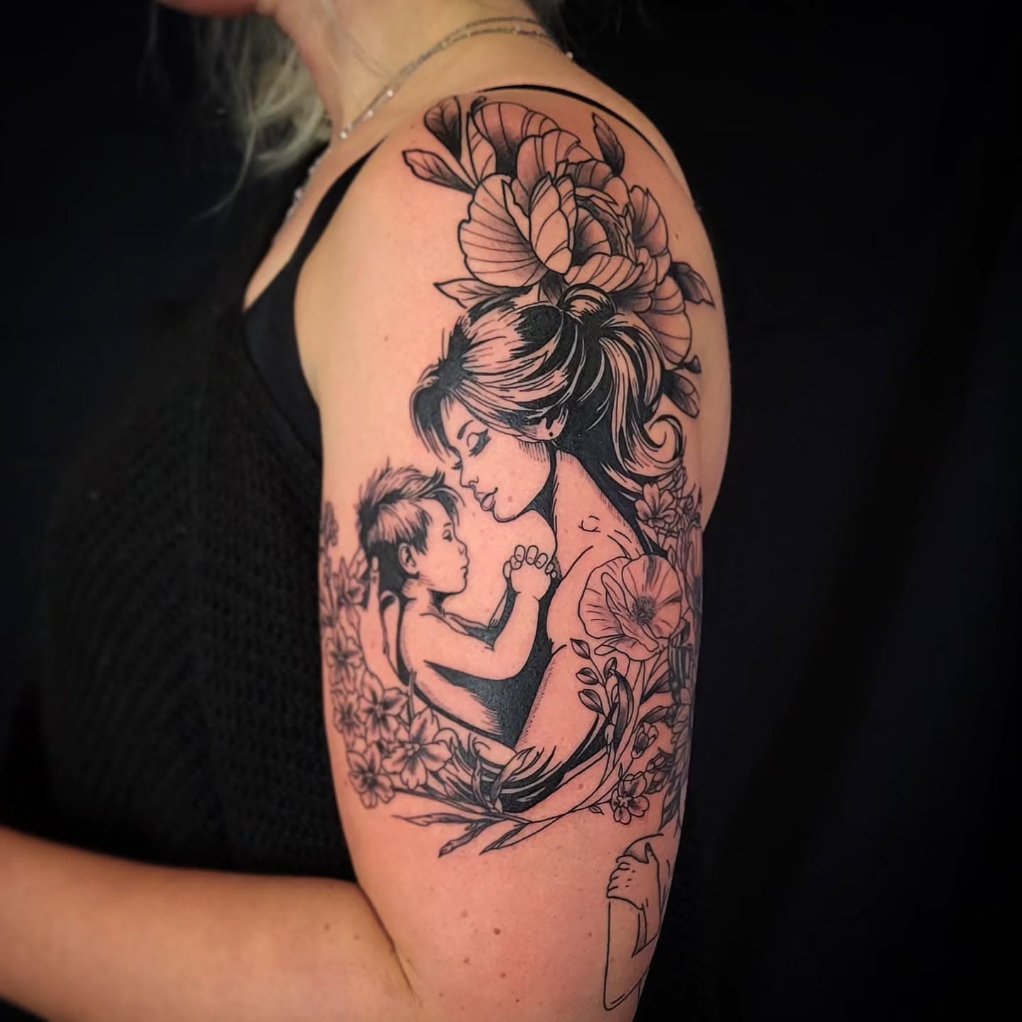 Blackwork tattoo van moeder met baby en bloemen op de bovenarm.