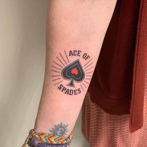 Ace of Spades tattoo met schoppensymbool en tekst op onderarm.