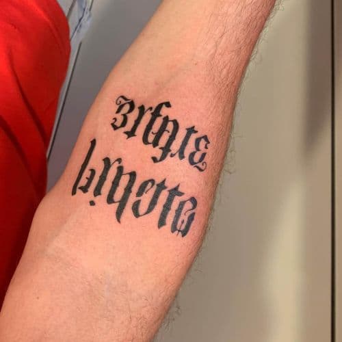 Gothic lettering tattoo 'Infinite Loyalty' op onderarm.
