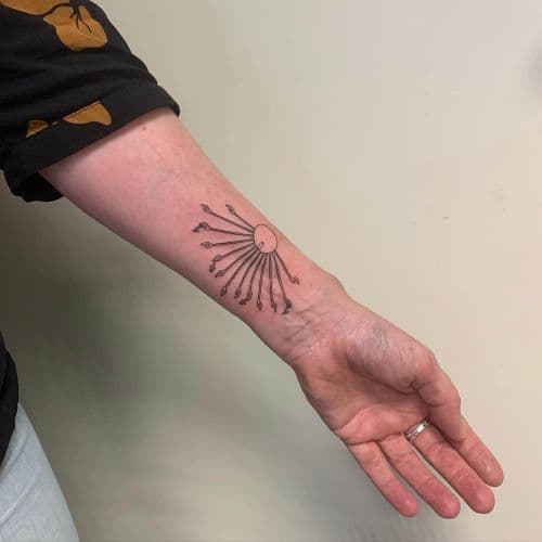 Minimalistische fineline tattoo van een zon met handen als stralen op de onderarm.