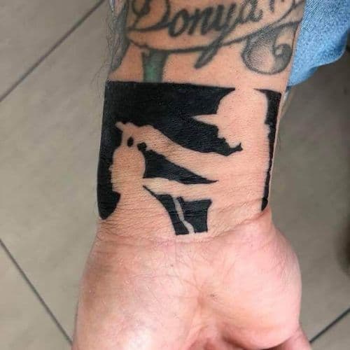 Zwart silhouet tattoo van een cowboy figuur op de pols.