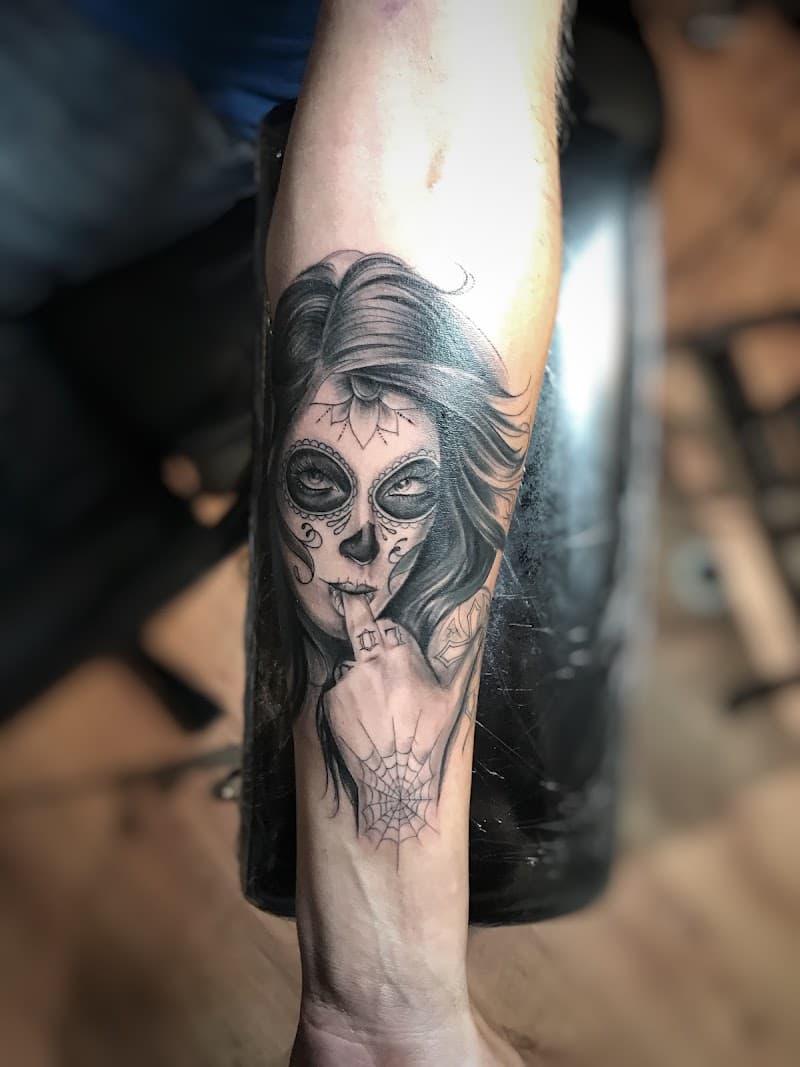 Zwart-wit tattoo van een vrouw met een suikerschedel gezicht en een vinger voor haar mond.