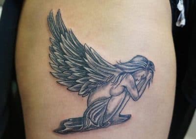 Zwart-wit tattoo van een knielende engel met grote vleugels.