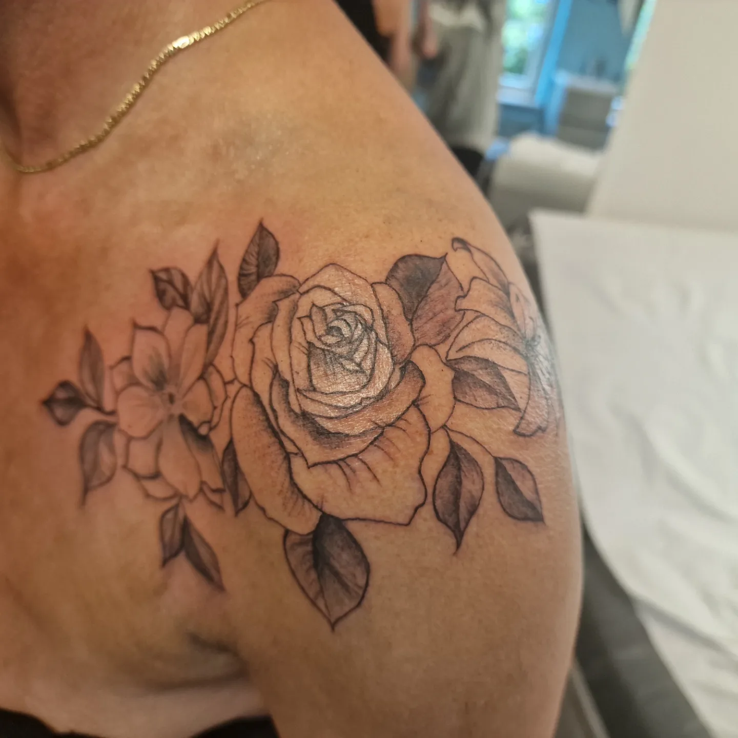Blackwork bloemen tattoo met roos en lelies op schouder.
