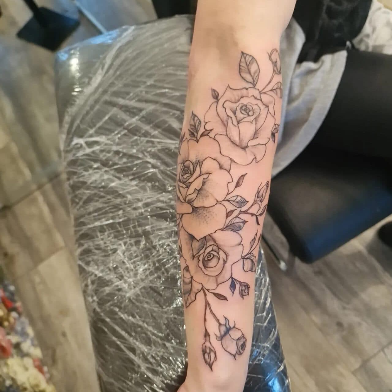 Fineline bloemen tattoo met rozen en bladeren op onderarm.