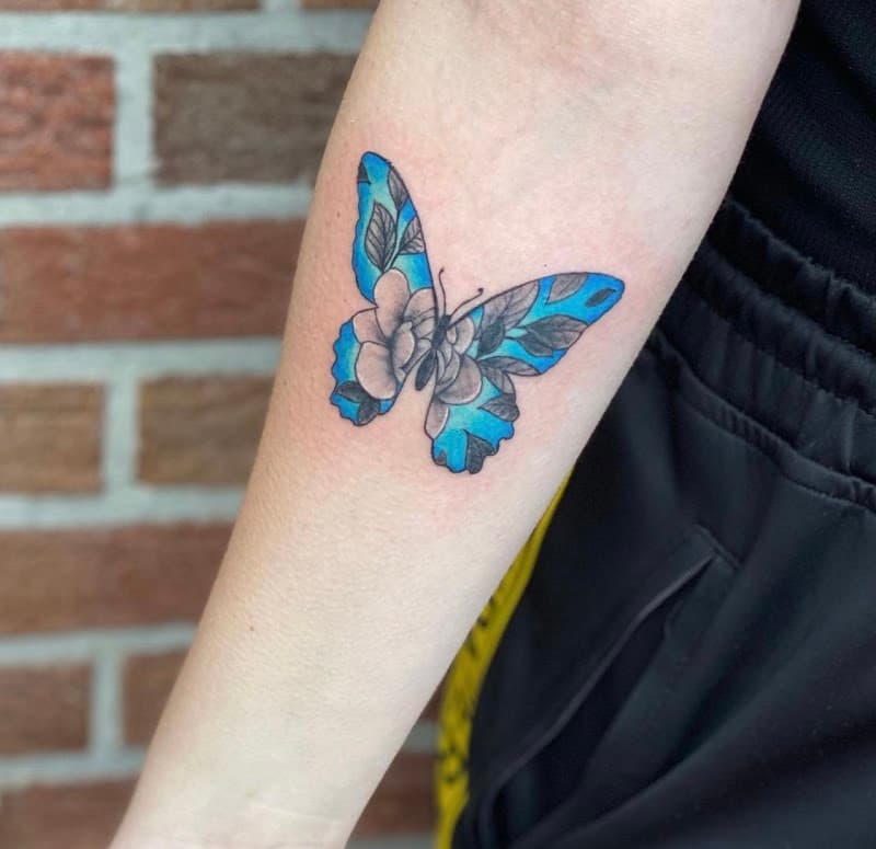 Blauwe vlinder met bloemenpatroon in vleugels op onderarm.