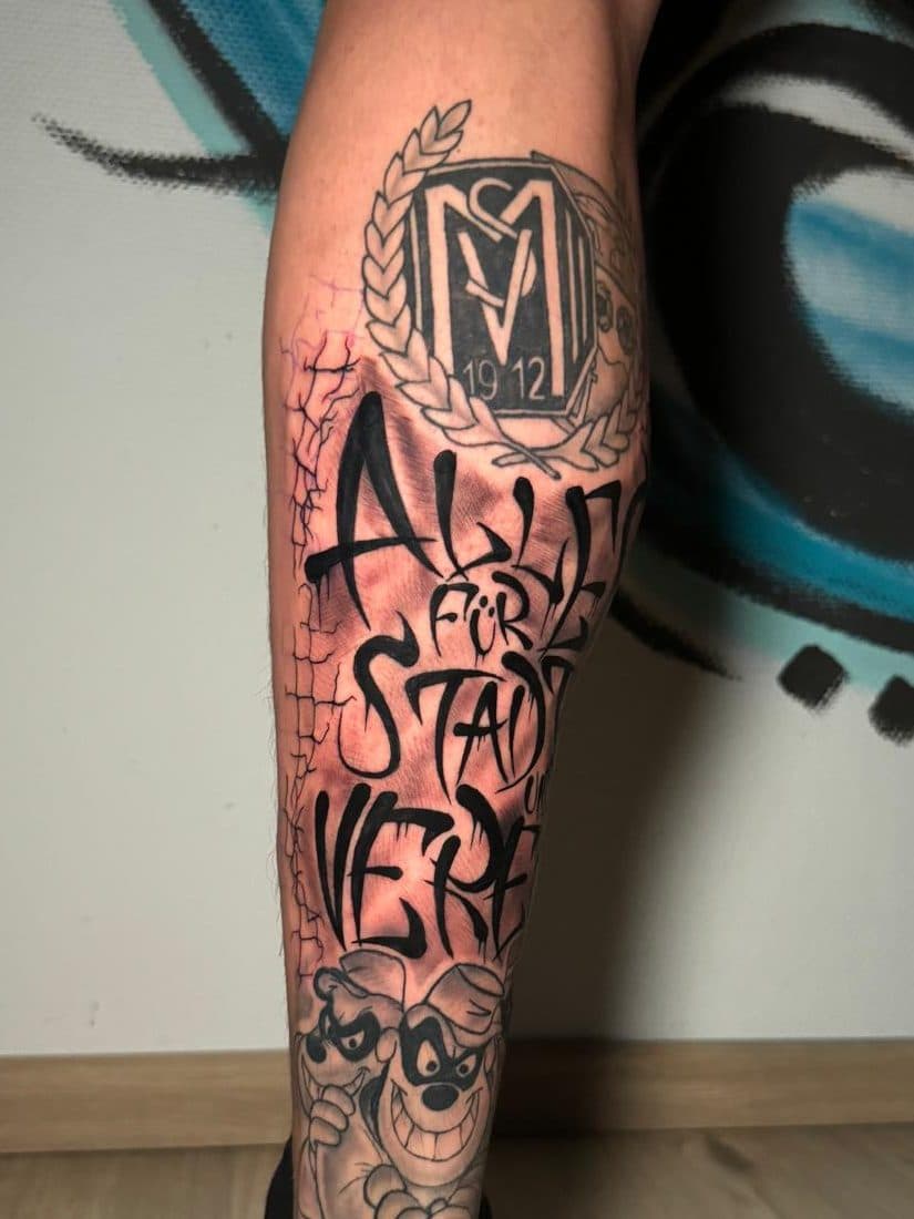 Grote blackwork tattoo op onderbeen met SV Meppen logo, graffiti tekst en cartoons.