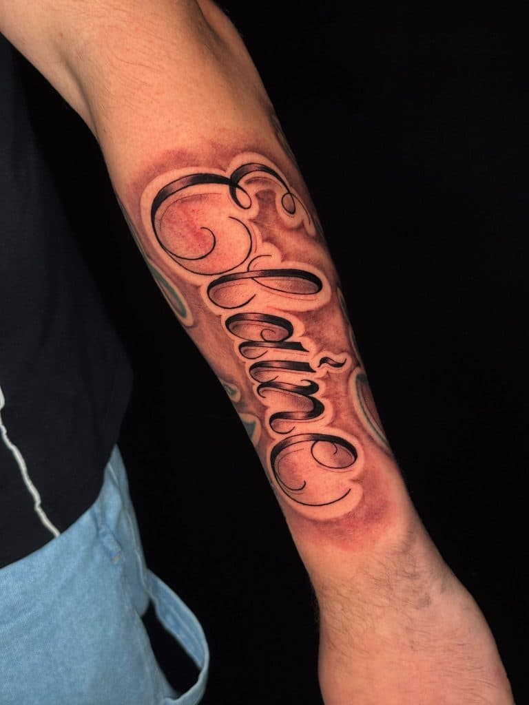 Sierlijke 'Elaine' naam tattoo in script op de onderarm.