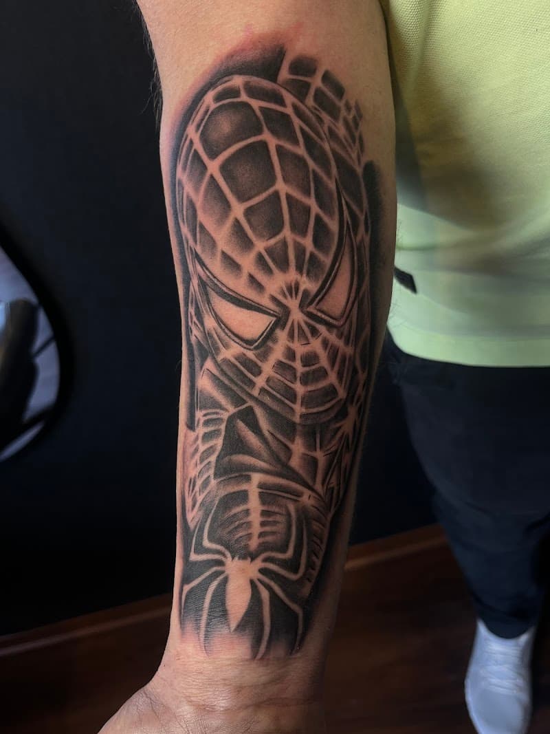 Zwart-wit Spider-Man masker en logo tattoo op onderarm.