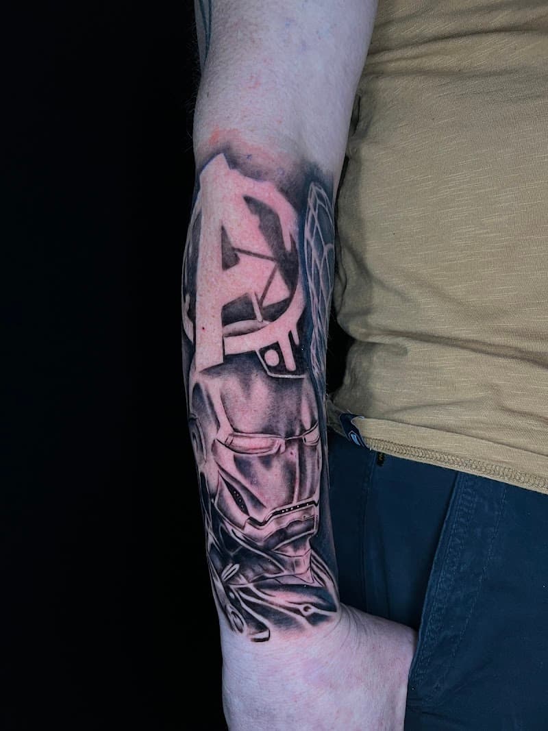 Zwart-wit tattoo van Iron Man en het Avengers logo op de onderarm.