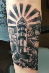 Zwart-wit tattoo van vuurtoren, schip en golven op onderarm.