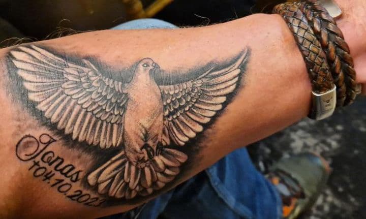 Zwart-grijze duif met naam 'Jonas' en datum '04.10.2023' op onderarm.